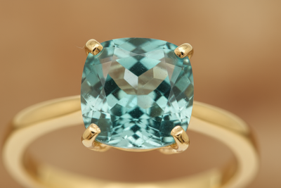 close-up of prongs holding in a light teal stone on a yellow gold ring 