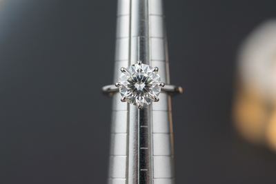 closeup of a 1ct solitaire diamond ring on a mandrel. darker blurred background